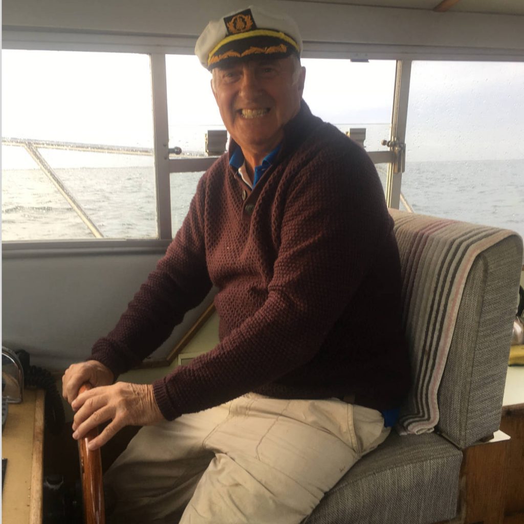 Alan Teasdale wearing a Captain's hat and steering a boat.